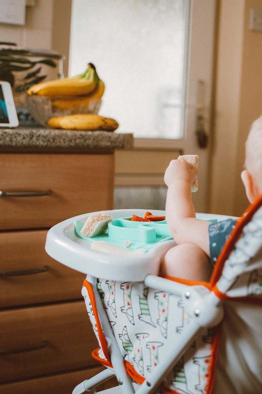 back view shot of a baby holding a food while sitting on a high chair